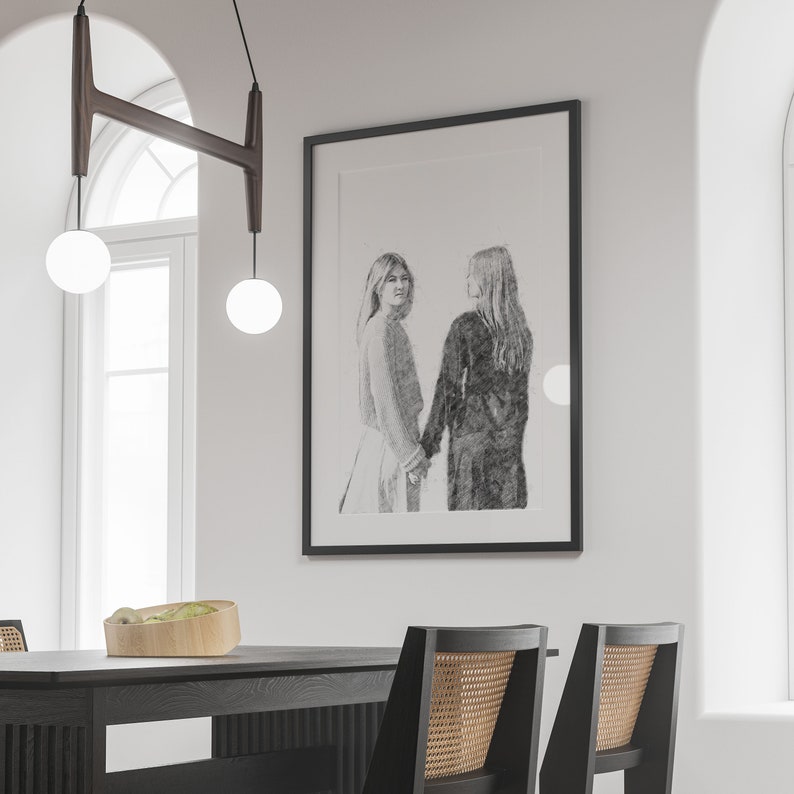 May include: A black framed drawing of two women standing side by side, holding hands. The drawing is in a minimalist style, with a white background and black lines.