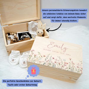 May include: A wooden baby keepsake box with the name "Emily" and birth details. The box is decorated with floral designs and contains baby items like booties, a stuffed bunny, and a wooden teether. The text on the box reads "26.12.2025 - 13:41 Uhr - 53 cm - 3100 g".