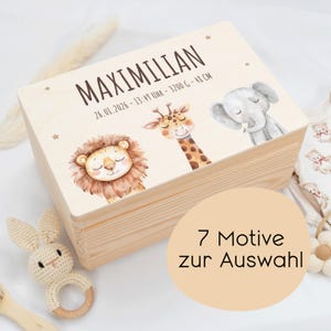 Pode incluir: Uma caixa de madeira clara com uma tampa com ilustrações de um leão, uma girafa e um elefante. A tampa também tem o nome "MAXIMILIAN" e detalhes do nascimento. Um adesivo redondo com o texto "7 Motive zur Auswahl" é visível.
