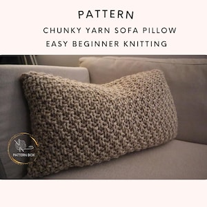 May include: A rectangular, chunky knit sofa pillow in a neutral beige color. The pillow is made with thick yarn and has a textured appearance. The image includes the text "PATTERN", "CHUNKY YARN SOFA PILLOW", and "EASY BEGINNER KNITTING".