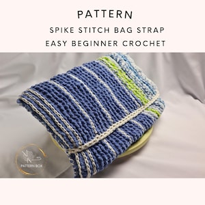 Puede incluir: Una correa de bolso de ganchillo azul y blanco con el texto "PATTERN SPIKE STITCH BAG STRAP EASY BEGINNER CROCHET". La correa tiene un diseño de puntada de espiga texturizada con rayas verticales blancas. La correa está doblada y parece estar sobre un plato verde claro.