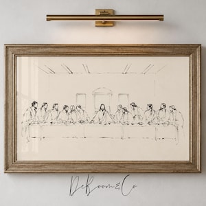 May include: A framed horizontal wall art print featuring a black ink line drawing of The Last Supper on a cream background. The artwork is displayed in a wooden frame with a brass-coloured picture light mounted directly above the frame on the wall.