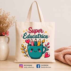 May include: A cream-colored canvas tote bag featuring a colorful graphic of a smiling teal mug filled with pencils and a paintbrush. The text reads Super &Eacute;ducatrice in pink and teal script. Decorative elements include yellow stars, pink hearts, and leafy branches.