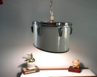 May include: A white drum converted into a hanging light fixture with a silver chain and a light bulb inside. The drum has silver hardware and a black rim.