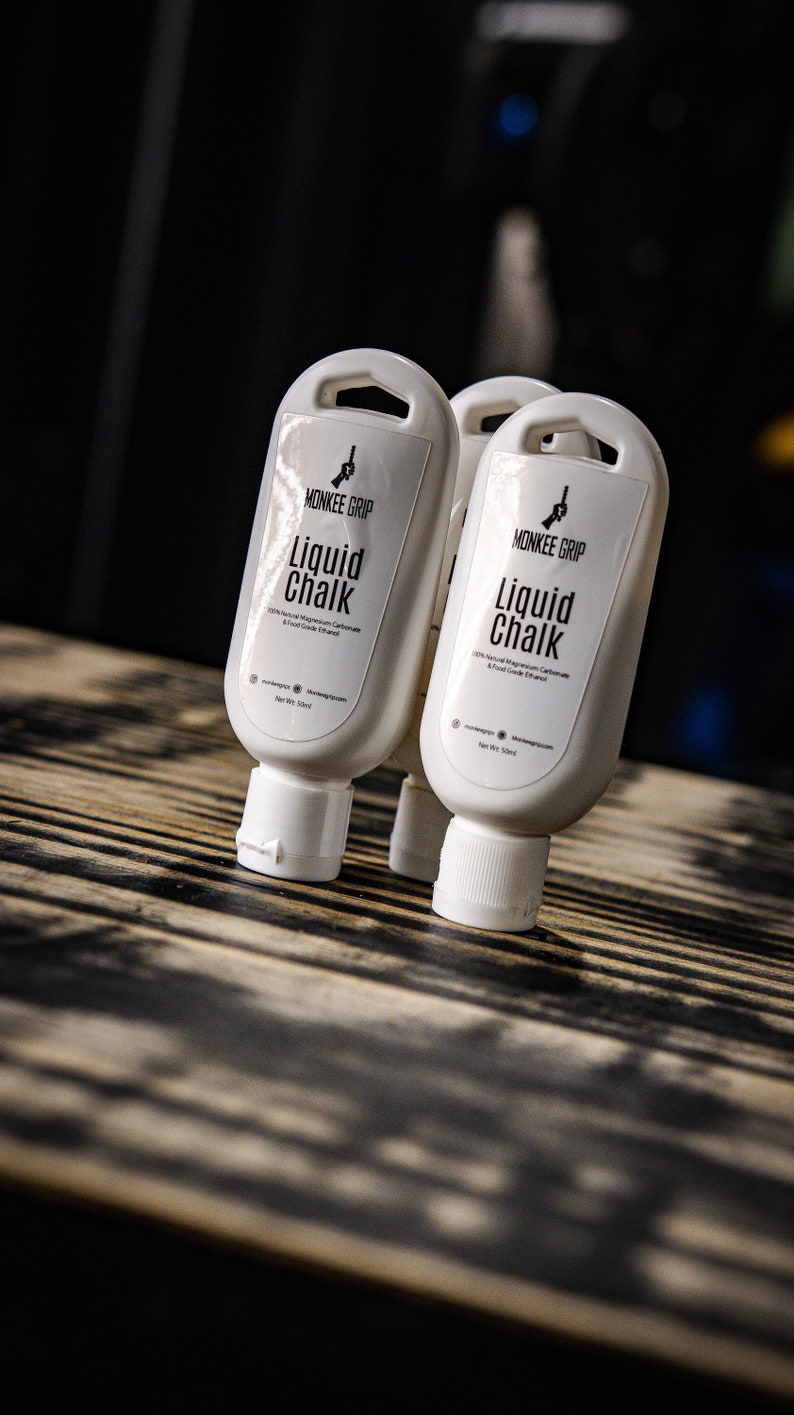 May include: Two white bottles of liquid chalk with black text that reads "MONKEE GRIP Liquid Chalk 100% Natural Magnesium Carbonate & Food Grade Ethanol Net Wt 5.2 fl oz (155ml)"