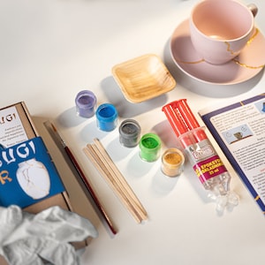 May include: Kintsugi repair kit with a broken teacup, epoxy adhesive, gold, blue, green, and purple powders, wooden sticks, a brush, and instructions. The kit includes everything needed to repair and decorate broken pottery.