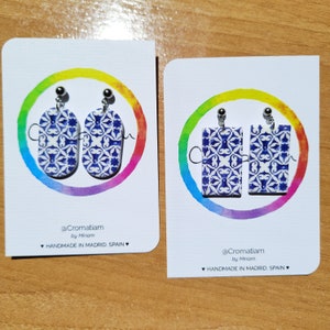 May include: Two pairs of earrings with blue and white patterned ceramic tiles. The earrings are on white cards with rainbow watercolor backgrounds. The cards have the text "@Cromatiam by Miriam HANDMADE IN MADRID, SPAIN".