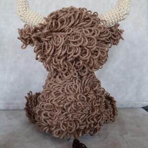 May include: A brown crocheted stuffed animal resembling a Highland cow with white horns and a brown tail.