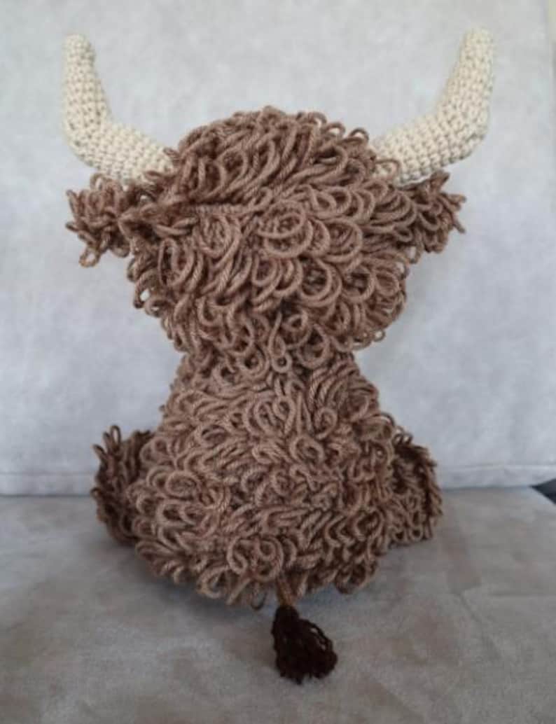 May include: A brown crocheted stuffed animal resembling a Highland cow with white horns and a brown tail.
