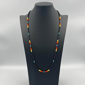 May include: A long black beaded necklace with colorful accents. The necklace features small beads in red, orange, yellow, turquoise, and white.
