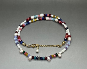May include: A multi-colored beaded necklace with white pearls, red, blue, green, and purple beads. The necklace has a gold clasp.