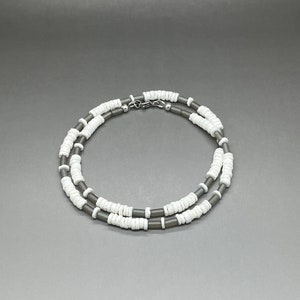 May include: A double-strand necklace made of gray and white beads. The necklace is made of small, round beads that are strung together in a repeating pattern.