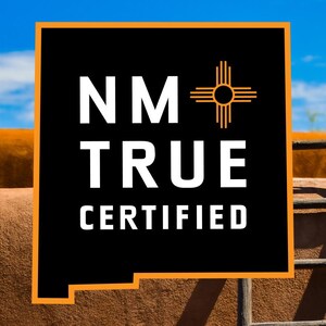 May include: A black and orange sign with the text "NM TRUE CERTIFIED" and a stylized symbol of the sun with rays.
