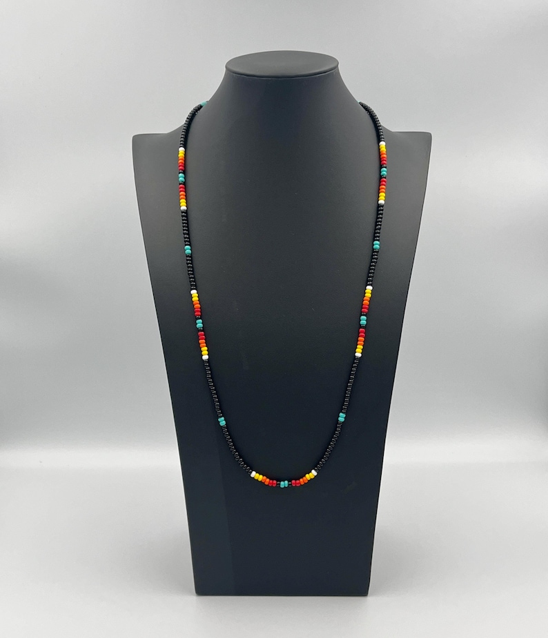 May include: A long black beaded necklace with colorful accents. The necklace features small beads in red, orange, yellow, turquoise, and white.