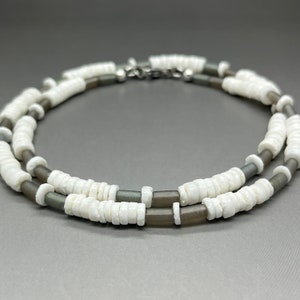 May include: A double-strand necklace made of white and gray beads. The necklace is made of two different types of beads, one white and one gray. The beads are all round and have a smooth finish.