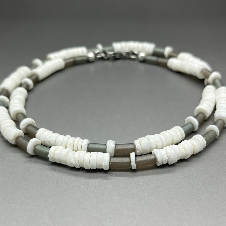 May include: A double-strand necklace made of white and gray beads. The necklace is made of two different types of beads, one white and one gray. The beads are all round and have a smooth finish.