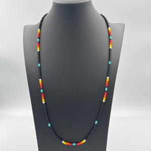 May include: A black beaded necklace with colorful accents. The necklace features small, black beads with alternating red, orange, yellow, turquoise, and white beads.