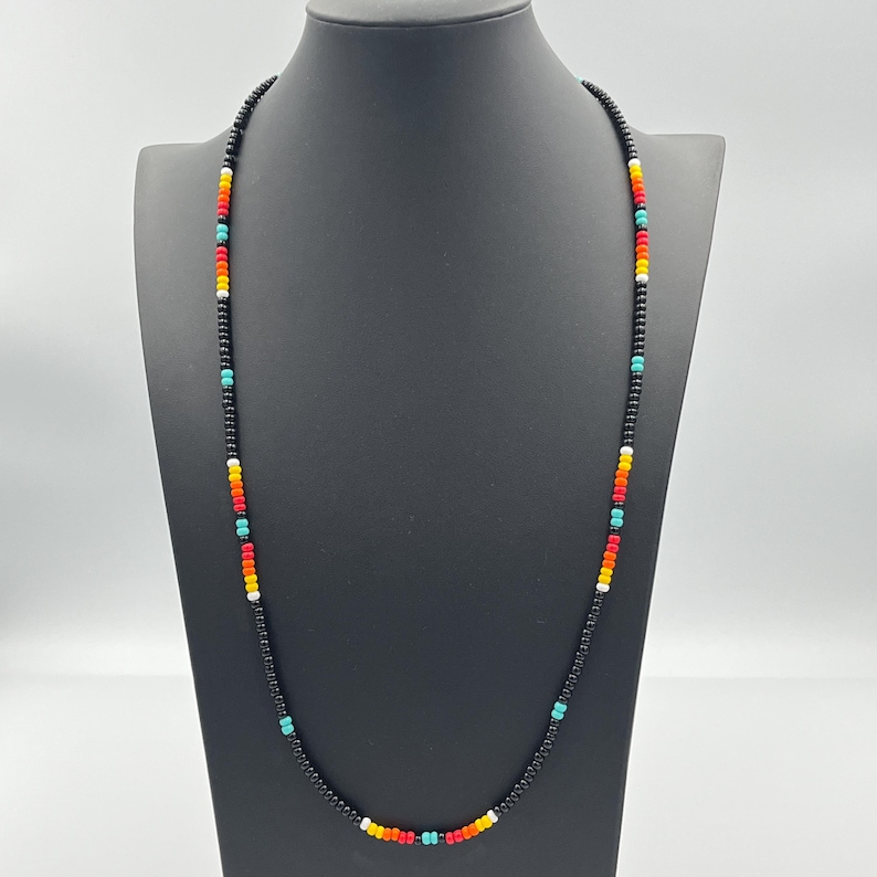 May include: A black beaded necklace with colorful accents. The necklace features small, black beads with alternating red, orange, yellow, turquoise, and white beads.