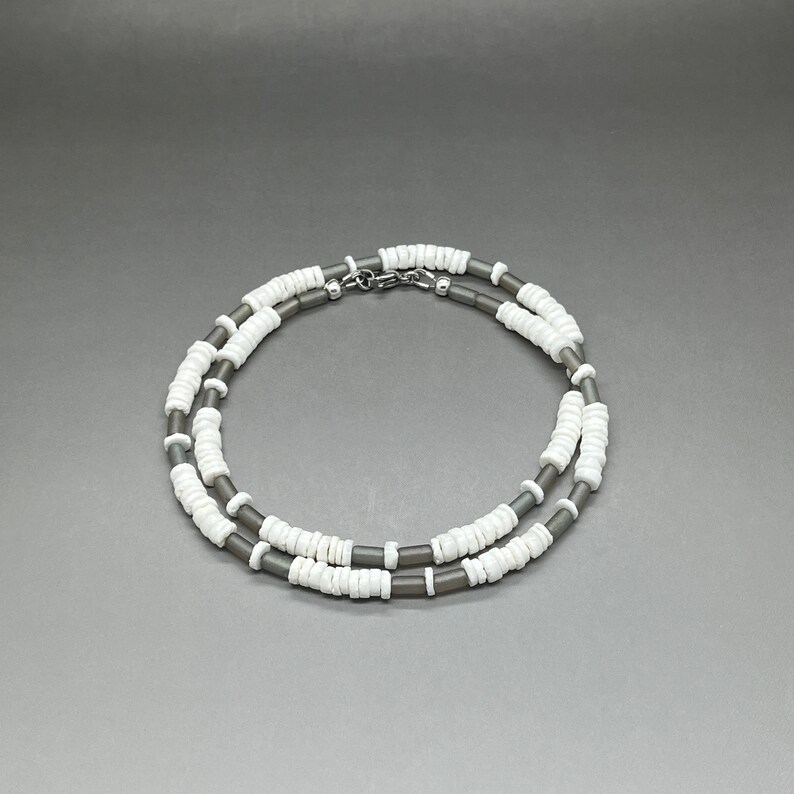 May include: A double-strand necklace made of gray and white beads. The necklace is made of small, round beads that are strung together in a repeating pattern.