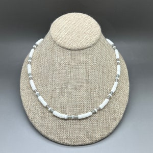 May include: A white and gray beaded necklace on a fabric-covered mannequin.