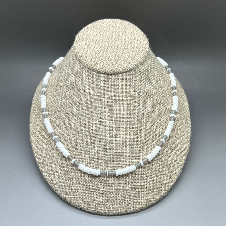 May include: A white and gray beaded necklace on a fabric-covered mannequin.