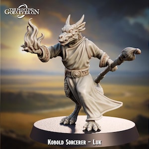 Puede incluir: Una figura miniatura pintada de un hechicero kobold, un humanoide reptiliano con una cola larga, que lleva una túnica y sostiene un bastón con una llama en el extremo. La figura está de pie sobre una base negra con el texto "Kobold Sorcerer - Luk" impreso en ella.