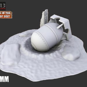May include: A 3D-printed model of a bomb, resting in a crater on a snow-like base. The model is light gray, with a cylindrical body and a fin-like structure. The base includes the text "Oasis in the Sea of Dirt" and "32MM".