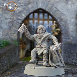 Puede incluir: Una miniatura de un enano barbudo impresa en 3D en gris, sosteniendo una jarra y sentado en un taburete. El enano lleva una túnica y una capa. La miniatura está sobre una base redonda.