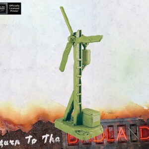 Puede incluir: Un modelo de turbina eólica de plástico verde con una escalera y una pequeña caja en la base. El modelo está sobre una superficie texturizada con las palabras "Return To The Badlands" visibles en el fondo.