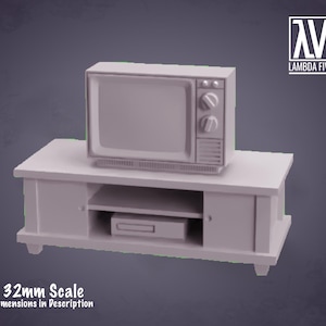 Puede incluir: Un televisor gris de estilo vintage en un mueble de entretenimiento gris a juego con un estante y dos puertas. El televisor tiene una pantalla negra y dos botones en la parte delantera. El mueble de entretenimiento es a escala de 32 mm.