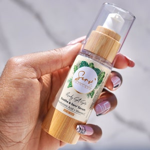 Puede incluir: Una botella de vidrio transparente con una tapa de bamb&uacute; y un dispensador de bomba blanco. La botella est&aacute; etiquetada con "Serv' Skincare" y "Ready Set Serv' Soothe & Serv' Serum Hyaluronic Acid + Vitamin C" con un peso neto de 30 ml.