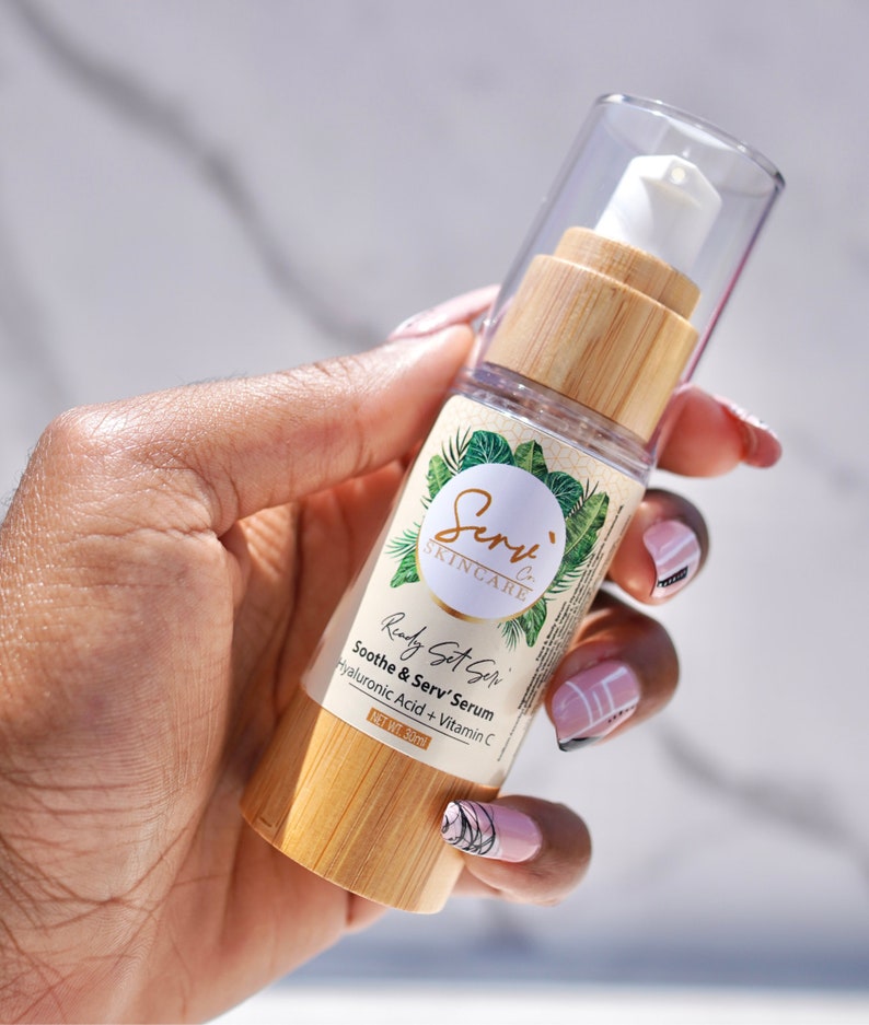 Puede incluir: Una botella de vidrio transparente con una tapa de bamb&uacute; y un dispensador de bomba blanco. La botella est&aacute; etiquetada con "Serv' Skincare" y "Ready Set Serv' Soothe & Serv' Serum Hyaluronic Acid + Vitamin C" con un peso neto de 30 ml.