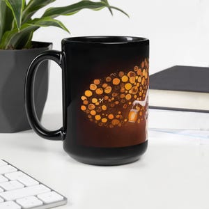 May include: Black ceramic mug featuring a whimsical illustration of a figure holding a lantern, with a cluster of golden orbs. The design is set against a gradient background of brown and gold. The mug has a large handle.