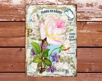 May include: A vintage-style sign with a white rose and green leaves on a blue background. The sign reads "Fleur de Roses", "Paris", "Perfumeur", "White Rose Beauty", and "Paul & Harvet".