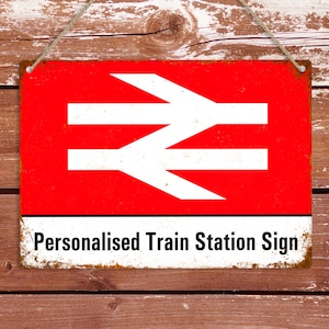 以下が含まれることがあります： イギリス国鉄のロゴと「パーソナライズされた駅名標識」という文字が書かれた赤と白の金属製の標識。標識は紐で吊り下げられており、素朴で風化した外観をしています。