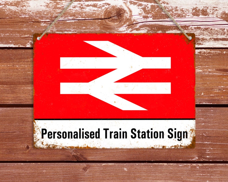 May include: A red and white metal sign with the British Rail logo and the text "Personalised Train Station Sign". The sign is hanging from a string and has a rustic, weathered look.