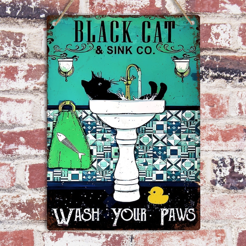 K&ouml;nnte beinhalten: Ein Vintage-Schild aus Metall mit einer schwarzen Katze, die sich in einem wei&szlig;en Waschbecken mit Sockel w&auml;scht. Das Schild hat einen t&uuml;rkisfarbenen Hintergrund mit wei&szlig;en und blauen Fliesenmustern. Der Text auf dem Schild lautet "Black Cat & Sink Co. Wash Your Paws".
