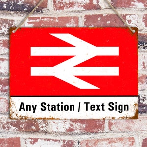 May include: A red and white metal sign with the text "Any Station / Text Sign" and a white stylized logo of a railway symbol. The sign has a distressed, rusty look.