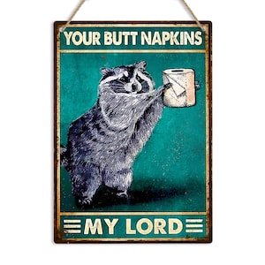 May include: A rectangular metal sign featuring a raccoon presenting a toilet roll. The sign reads "YOUR BUTT NAPKINS" and "MY LORD". The background is teal with a distressed effect, and the sign is framed in a rustic style.