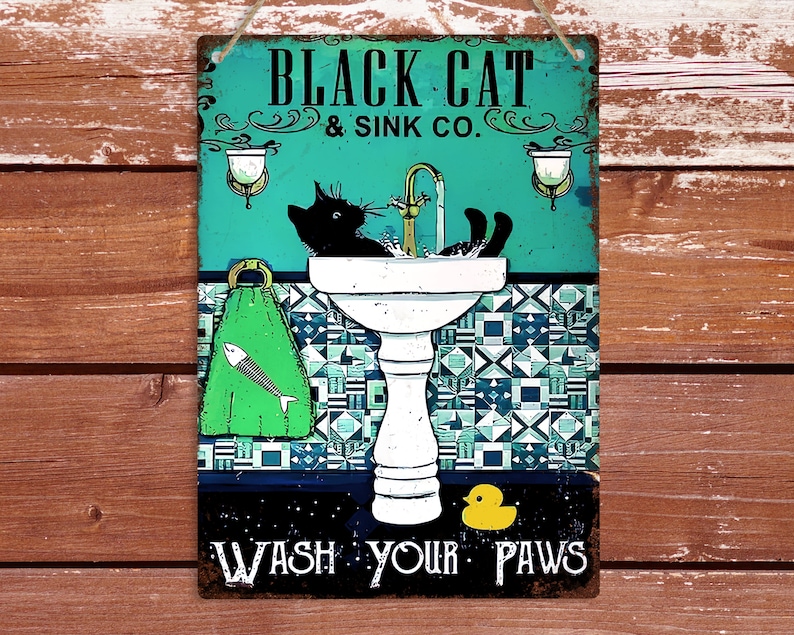 K&ouml;nnte beinhalten: Ein blaues und wei&szlig;es Schild mit dem Text "Black Cat & Sink Co." und einer schwarzen Katze, die sich in einem wei&szlig;en Porzellanwaschbecken w&auml;scht. Das Schild tr&auml;gt auch den Text "Wash Your Paws" und eine gelbe Gummiente.