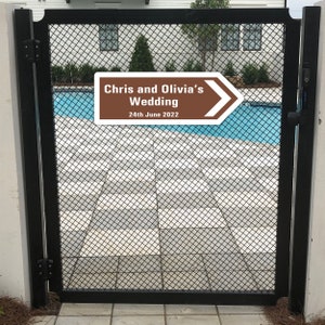 Puede incluir: Un cartel marr&oacute;n y blanco con una flecha que apunta hacia la derecha. El cartel dice "Chris and Olivia's Wedding 24th June 2022". El cartel est&aacute; sujeto a una puerta de metal negro.