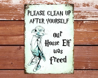 May include: A white metal sign with a green tint and a cartoon image of a house elf. The sign reads "Please clean up after yourself, our house elf was freed."