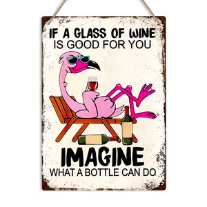 Puede incluir: Un flamenco rosa con gafas de sol y sosteniendo una copa de vino se relaja en una tumbona. El texto "IF A GLASS OF WINE IS GOOD FOR YOU IMAGINE WHAT A BOTTLE CAN DO" est&aacute; impreso en el cartel.