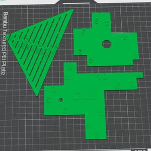 Puede incluir: Tres herramientas de plástico verde brillante impresas en 3D con números y marcas en relieve. Una es un triángulo grande con ranuras y dos son piezas irregulares en forma de cruz con orificios circulares sobre una rejilla gris.