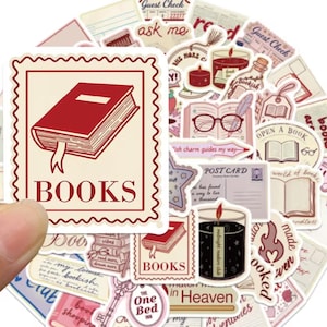 Peut inclure: Un ensemble d'autocollants découpés illustrant des thèmes littéraires dans des tons rouge, crème et marron. Les motifs incluent des livres, des bougies, des cartes postales et des lunettes avec le texte BOOKS, POST CARD et One More Chapter.