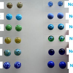 Puede incluir: Una colección de doce pares de pendientes de botón en varios colores y diseños. Los pendientes se muestran en tarjetas de plástico transparente con etiquetas. Los colores incluyen verde, azul, amarillo y patrones veteados. El texto "No:1" a "No:12" es visible.
