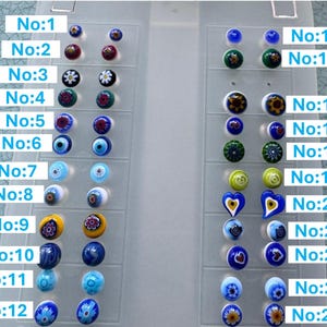 May include: A collection of 24 pairs of colorful glass beads, each with unique designs. The beads are arranged in a clear plastic organizer, showcasing various patterns and colors, including floral, geometric, and abstract designs.
