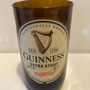 May include: A brown glass beer bottle with a label that reads "Traditionally Brewed", "Est. 1759", "Guinness Extra Stout", "5.6% Alc/Vol", "22 fl. oz.", "St. James's Gate Dublin", and "Arthur Guinness".