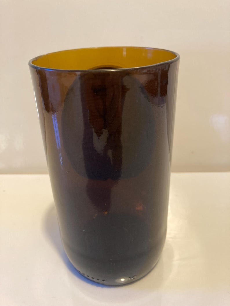 May include: A dark brown glass vase with a yellow rim. The vase is cylindrical in shape and has a smooth, glossy finish.