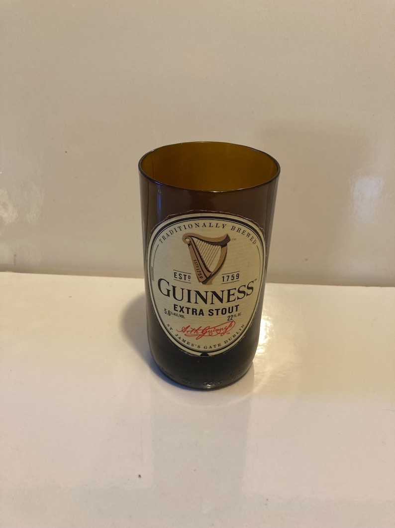 May include: A brown glass drinking glass with a Guinness Extra Stout label. The label features a harp and the text "Traditionally Brewed, Est. 1759, Guinness Extra Stout, St. James's Gate Dublin".